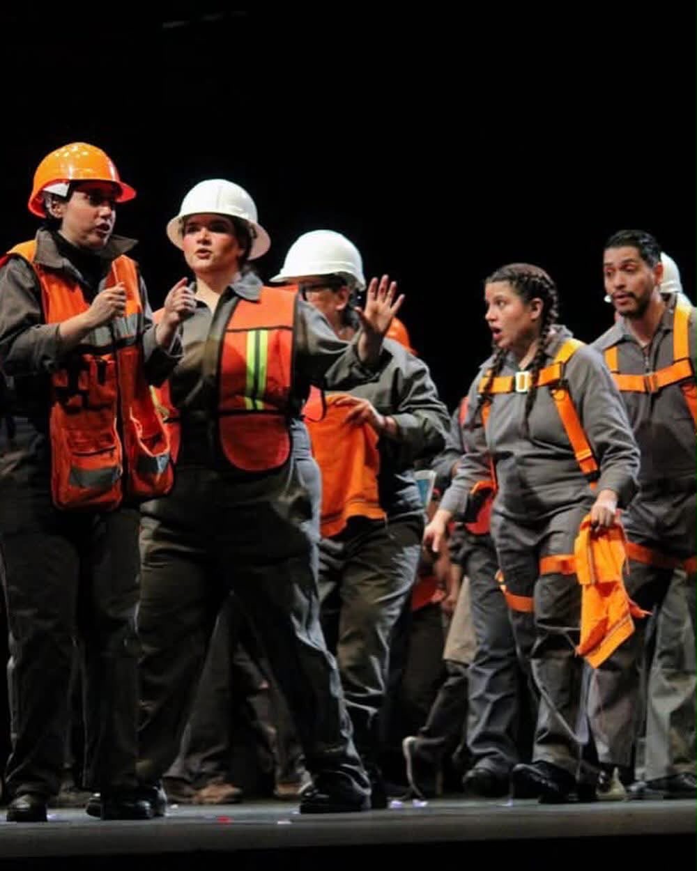 Escena de ópera contemporánea con el elenco caracterizado de obreros