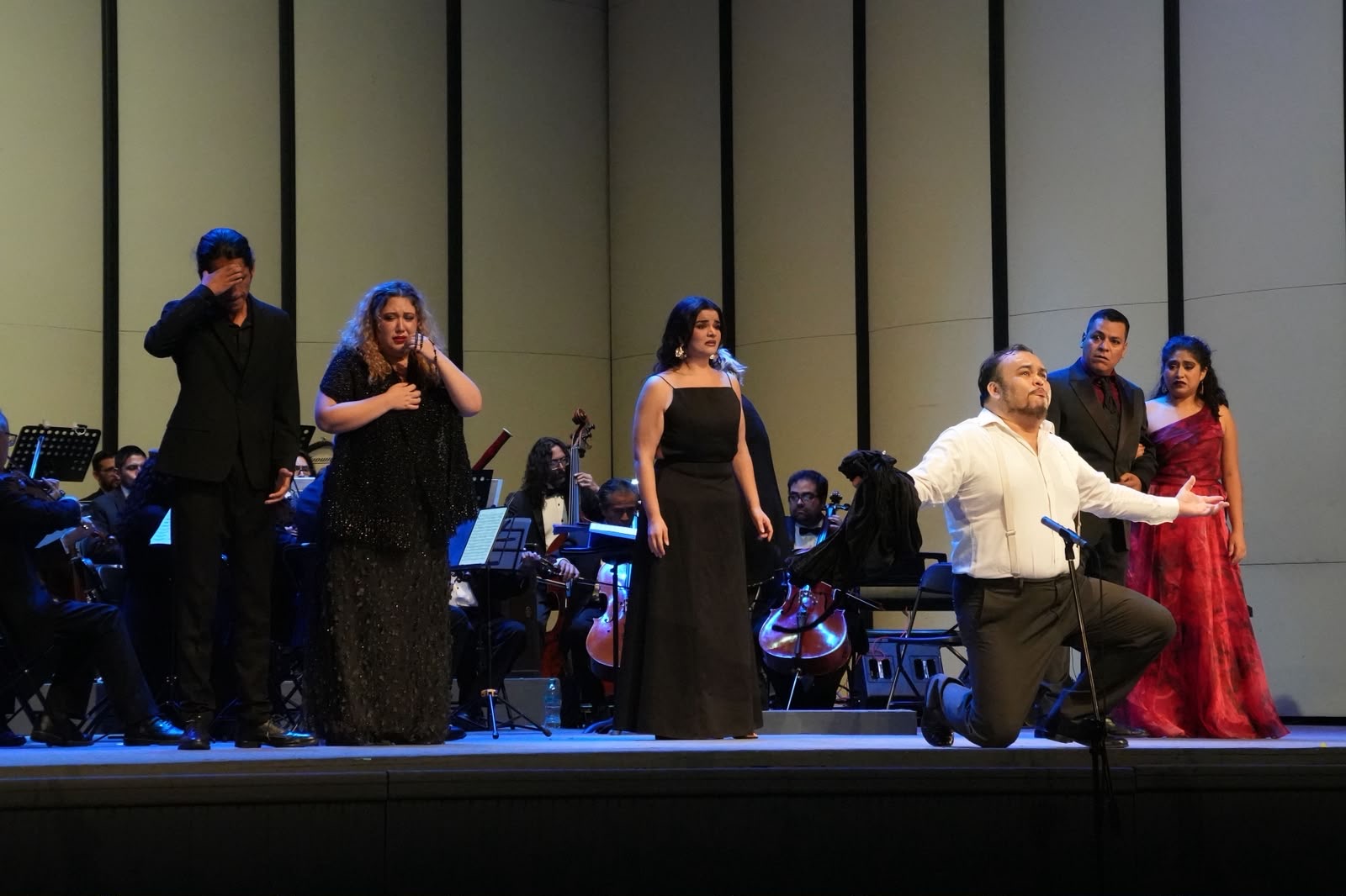 Escena dramática con cantantes y orquesta en vivo al fondo
