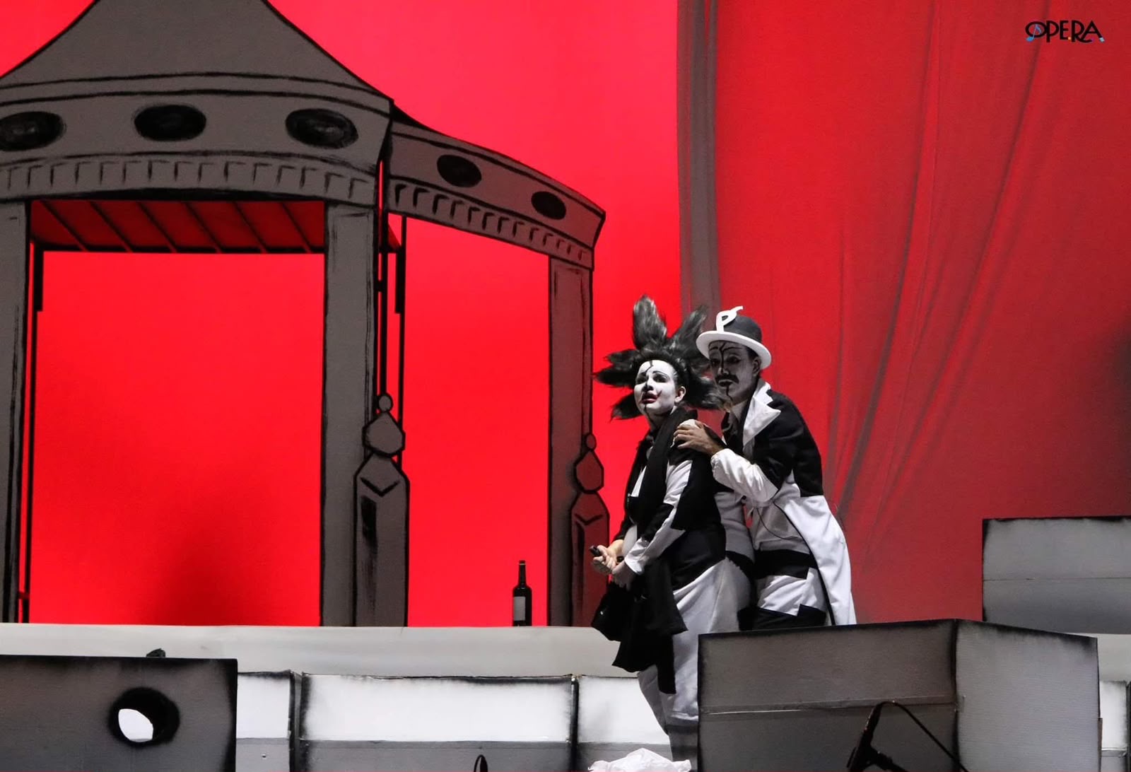 Escena de ópera con maquillaje blanco y fondo rojo intenso